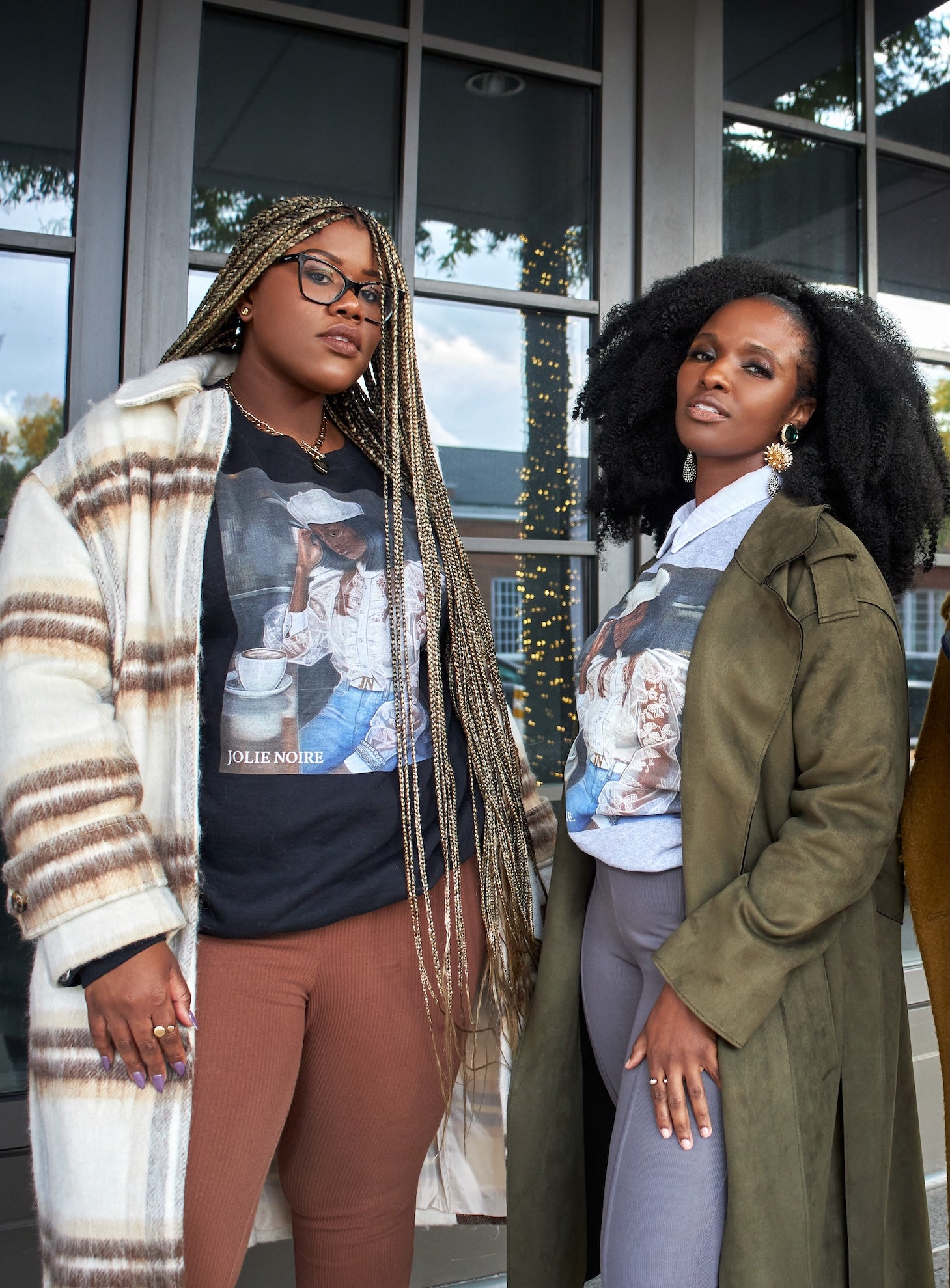 Two models standing outside a building, wearing casual outfits with graphic sweatshirts with girl in cafe design and jackets.