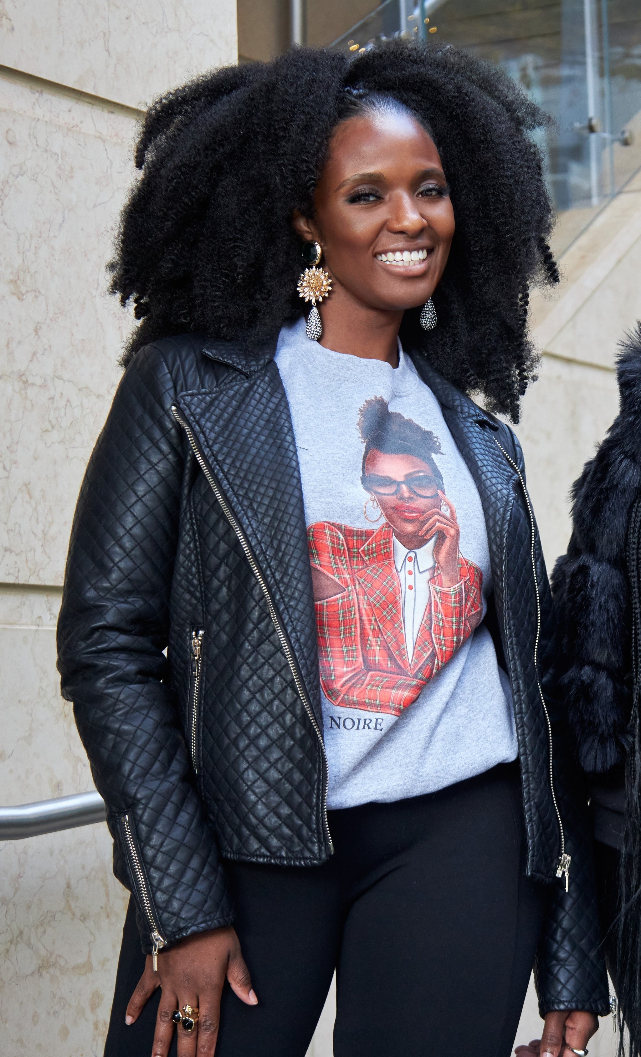 model wearing gray not so ugly christmas graphic sweatshirt with a leather jacket and black pants, standing outdoors.